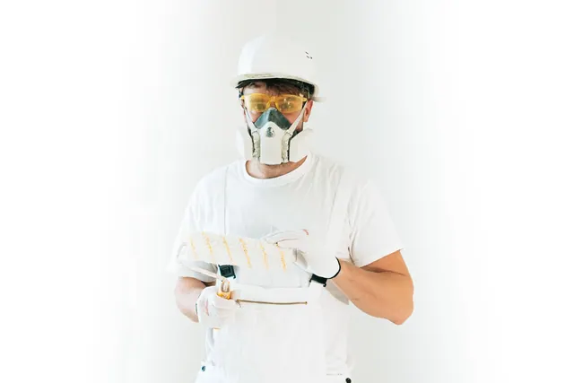 A professional painter wearing safety gear holding a paint roller, ready for work.